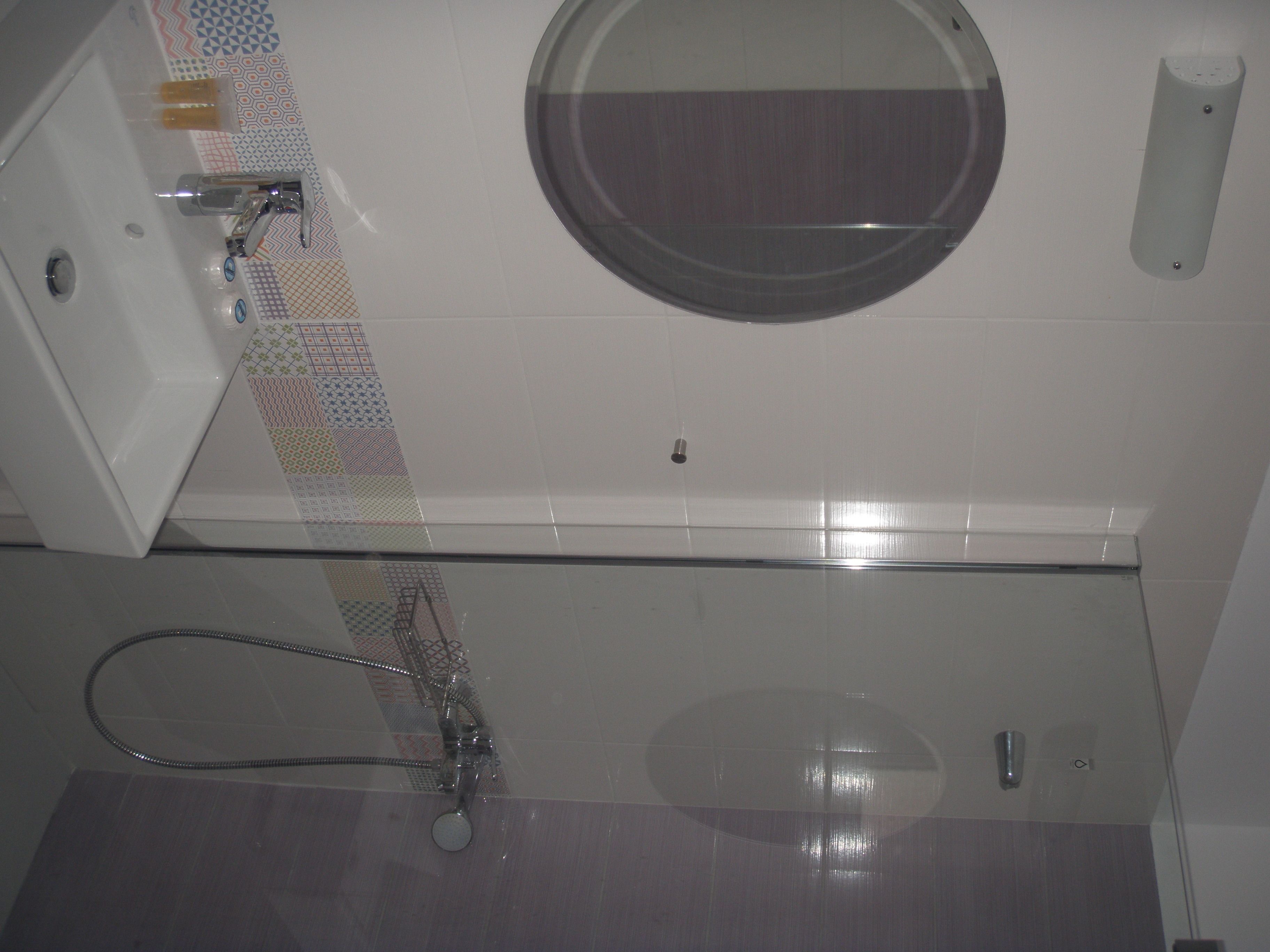 A bathroom with a glass shower enclosure, a round mirror, and a white sink.