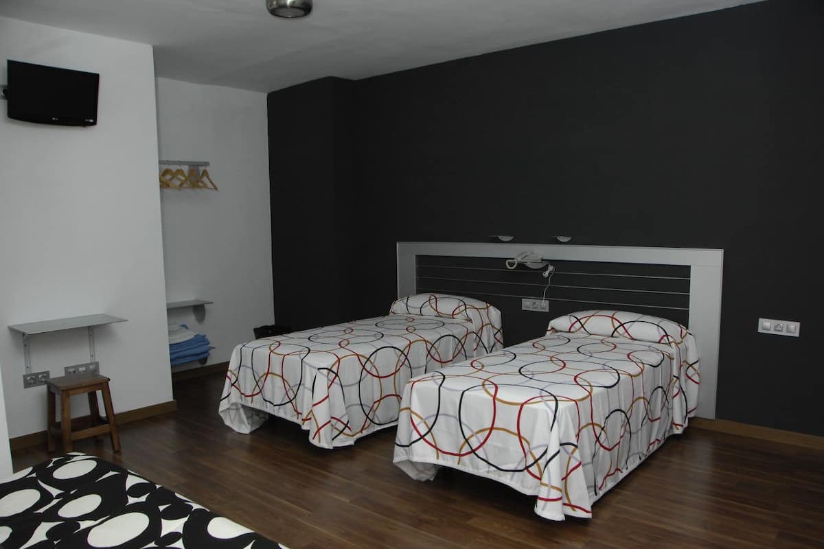 A room with two beds, a TV mounted on the wall, and a small table with a chair.