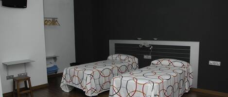 A room with two beds, a TV mounted on the wall, and a small table with a chair.