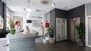 Uma área de recepção de hotel com balcão de atendimento, mapa na parede, extintor de incêndio e elevador.