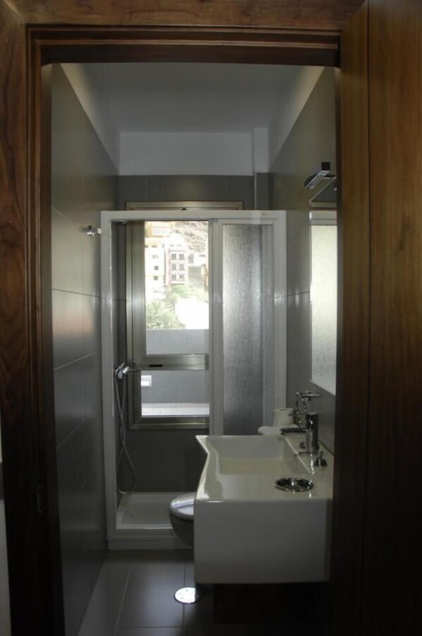 A modern bathroom with a shower, toilet, and sink, featuring a view of buildings outside. - La Colombina (San Sebastián de La Gomera)