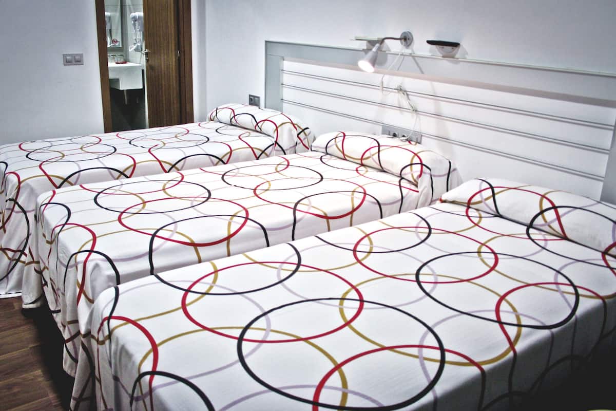A hotel room with two beds, each with a white bedspread featuring colorful circular patterns.
