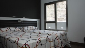 Quarto com uma janela ampla, cama com roupa de cama estampada e cabeceira preta.