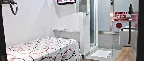 A hotel room with a bed, a TV mounted on the wall, a shower area, and a sign with instructions.