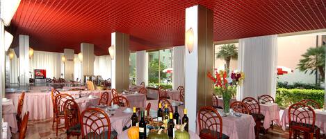 A restaurant with tables covered in pink tablecloths, wooden chairs, and a red ceiling.