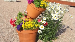 Una jardinera de terracota de varios niveles con diversas flores frente a un edificio de madera con balcón.