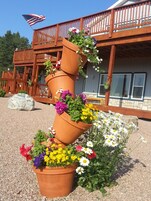Una jardinera de terracota de varios niveles con diversas flores frente a un edificio de madera con balcón.