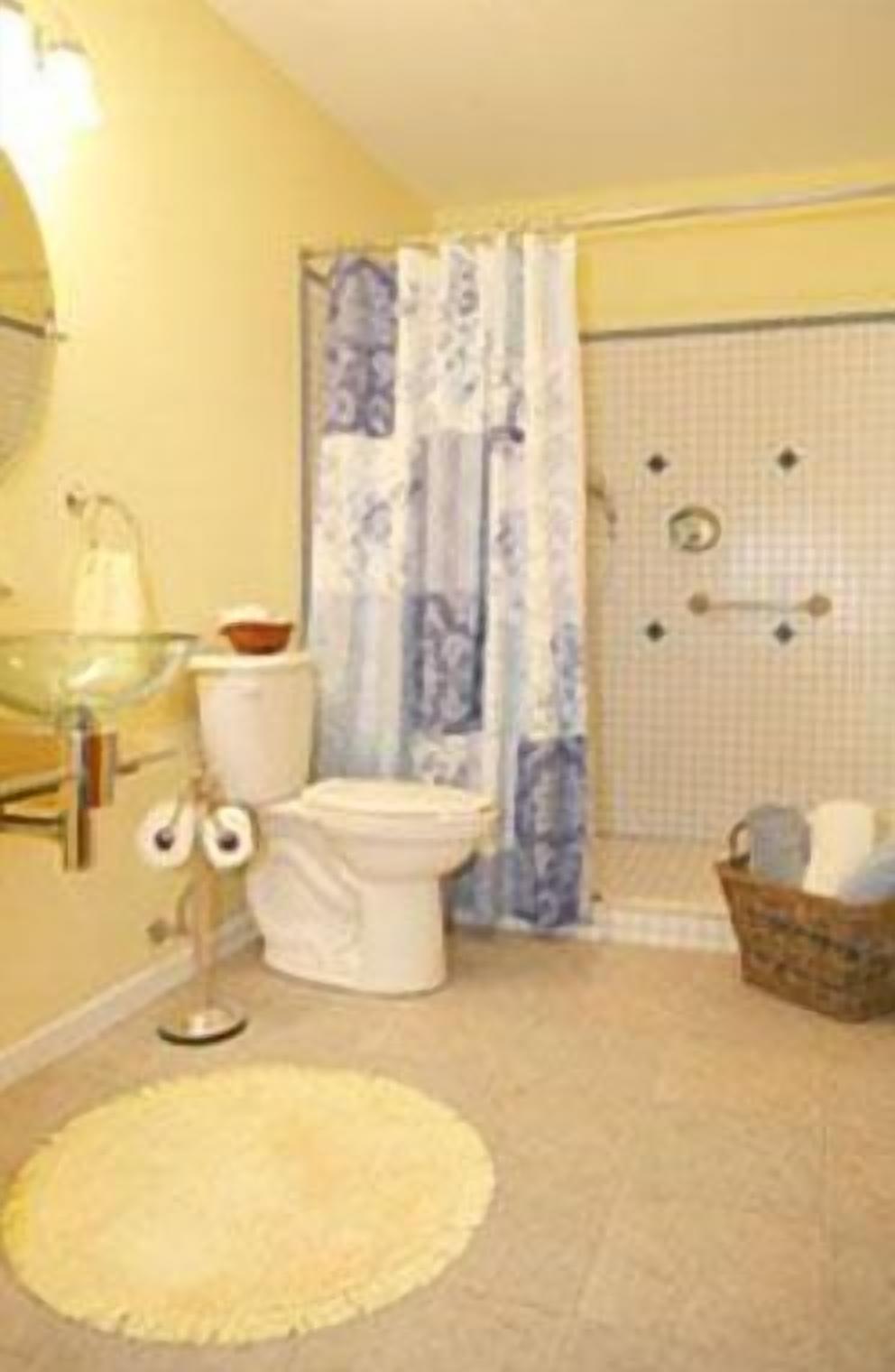 A bathroom with a toilet, a glass sink, a shower with a blue and white curtain, and a small wicker basket.