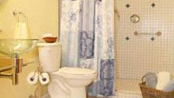 A bathroom with a toilet, a glass sink, a shower with a blue and white curtain, and a small wicker basket.