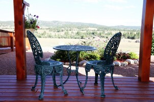 Una terraza de madera con dos sillas de metal decorativas y una mesa redonda, con vistas a un paisaje pintoresco.