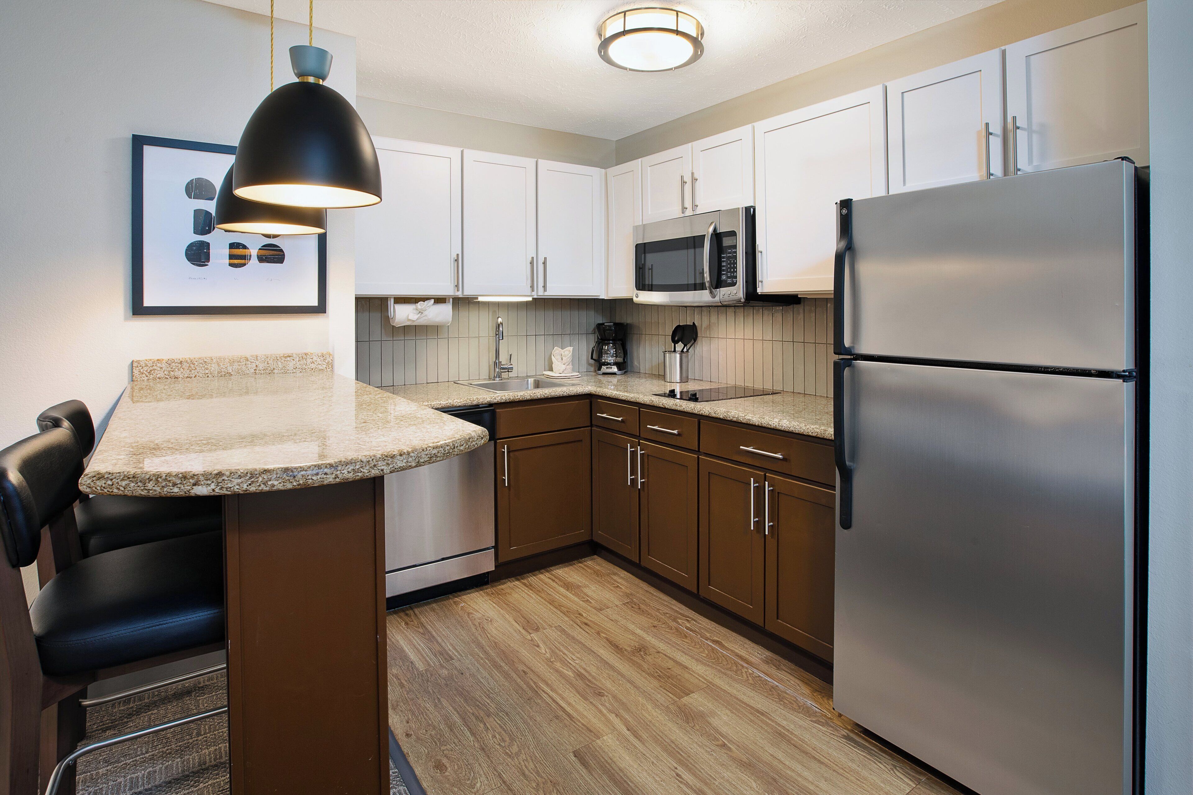 A modern kitchen with white cabinets, a stainless steel refrigerator, a microwave, and a granite countertop.