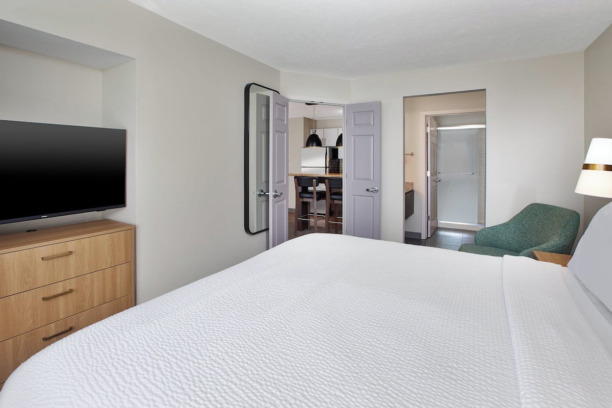 A hotel room with a large bed, a television on a wooden dresser, a green chair, and a walk-in closet.