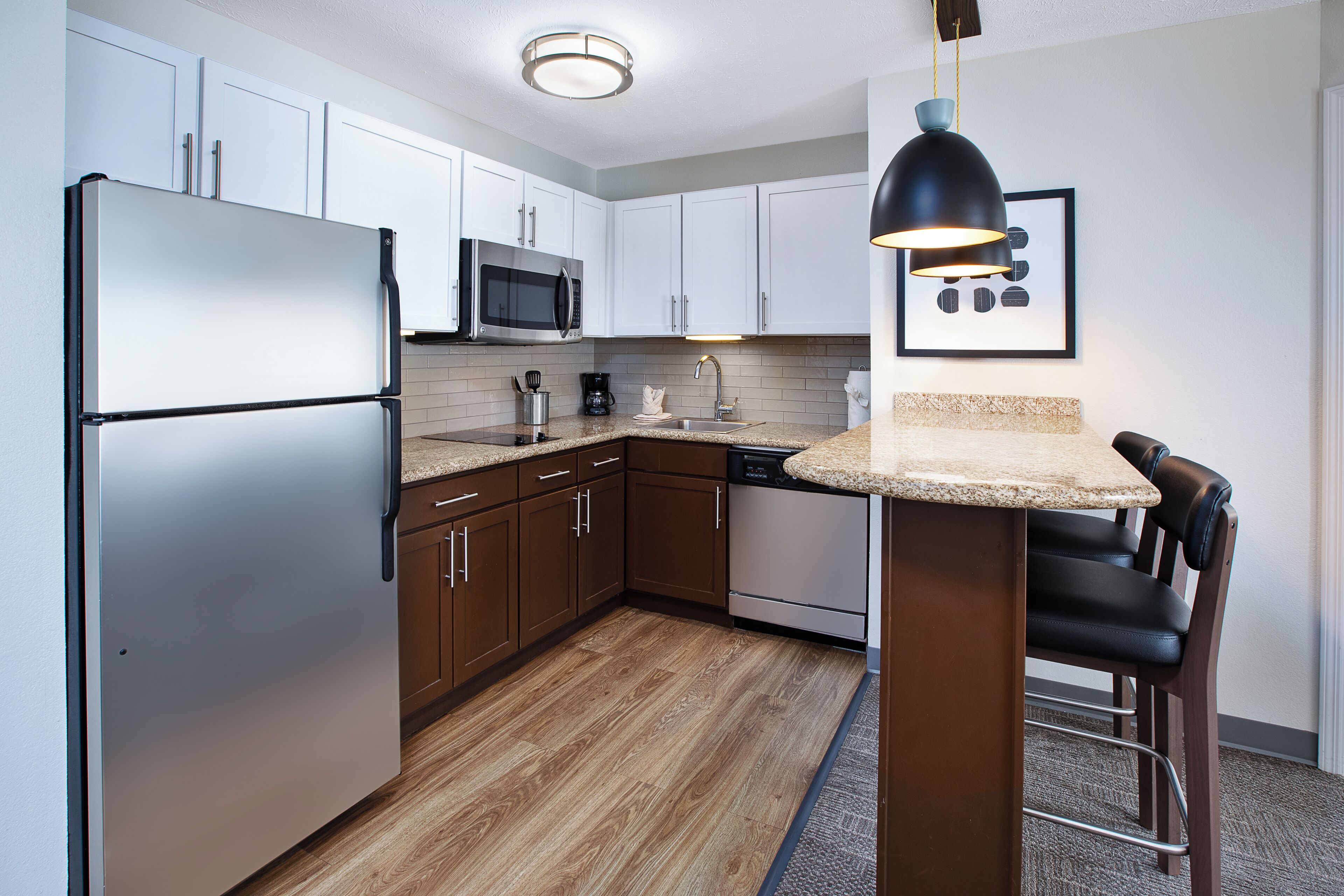 A modern kitchen with white cabinets, stainless steel appliances, a wooden floor, and a bar stool.