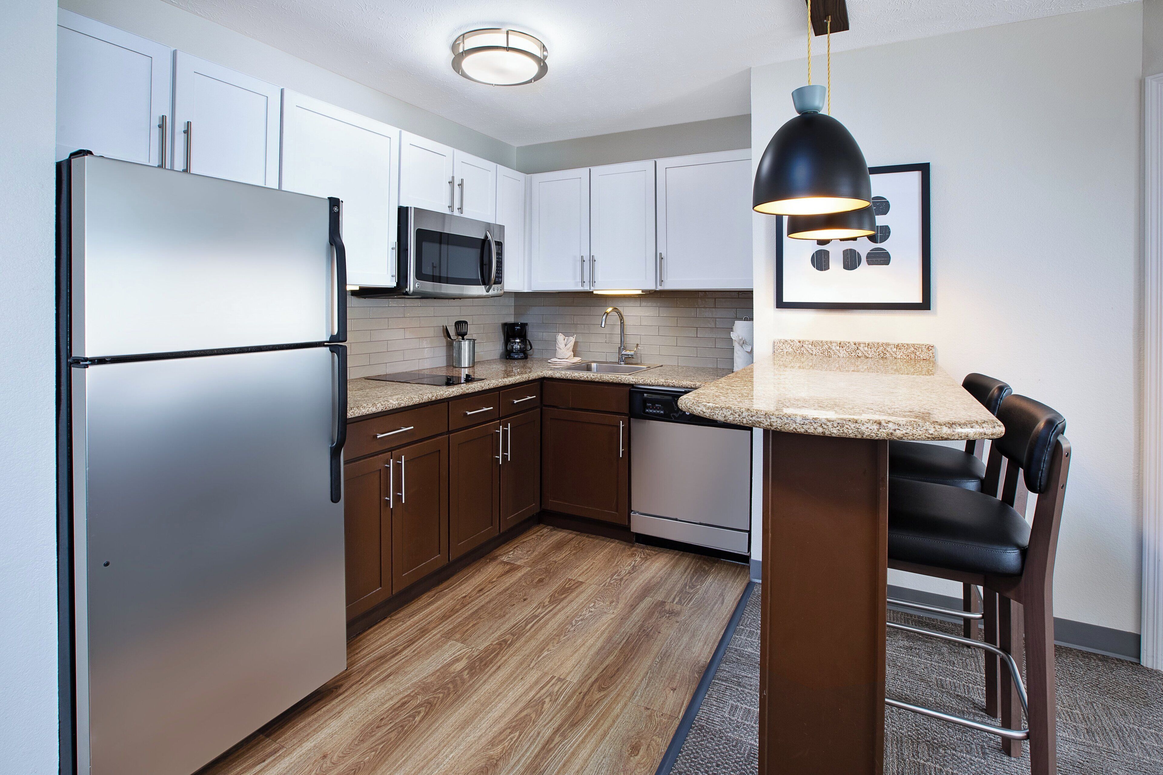A modern kitchen with white cabinets, stainless steel appliances, a wooden floor, and a bar stool.