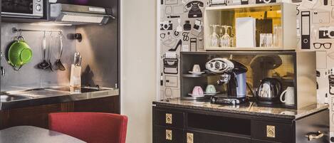 Una cocina compacta con electrodomésticos modernos, un comedor con una silla roja y una pared decorada con diversos objetos.