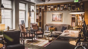 Een gezellige woonkamer met een bank, fauteuils, een salontafel en een boekenplank vol boeken.