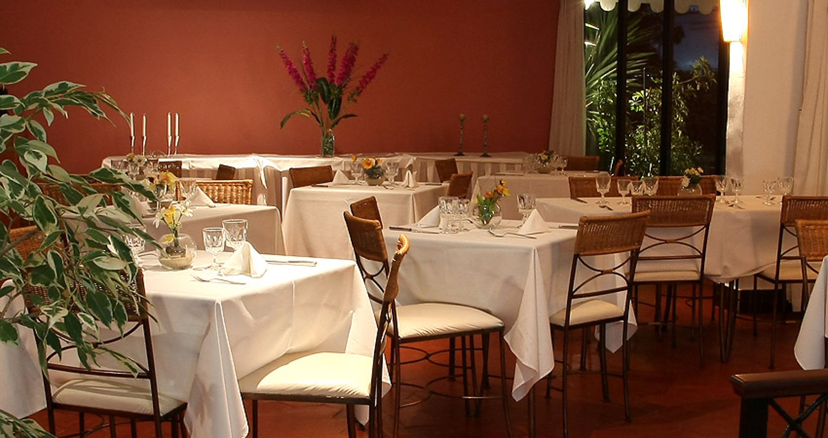 Un restaurante con varias mesas dispuestas para comer, con manteles blancos y sillas de mimbre.