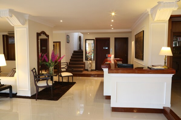 A hotel lobby with a reception desk, seating area, staircase, and a large framed picture on the wall.