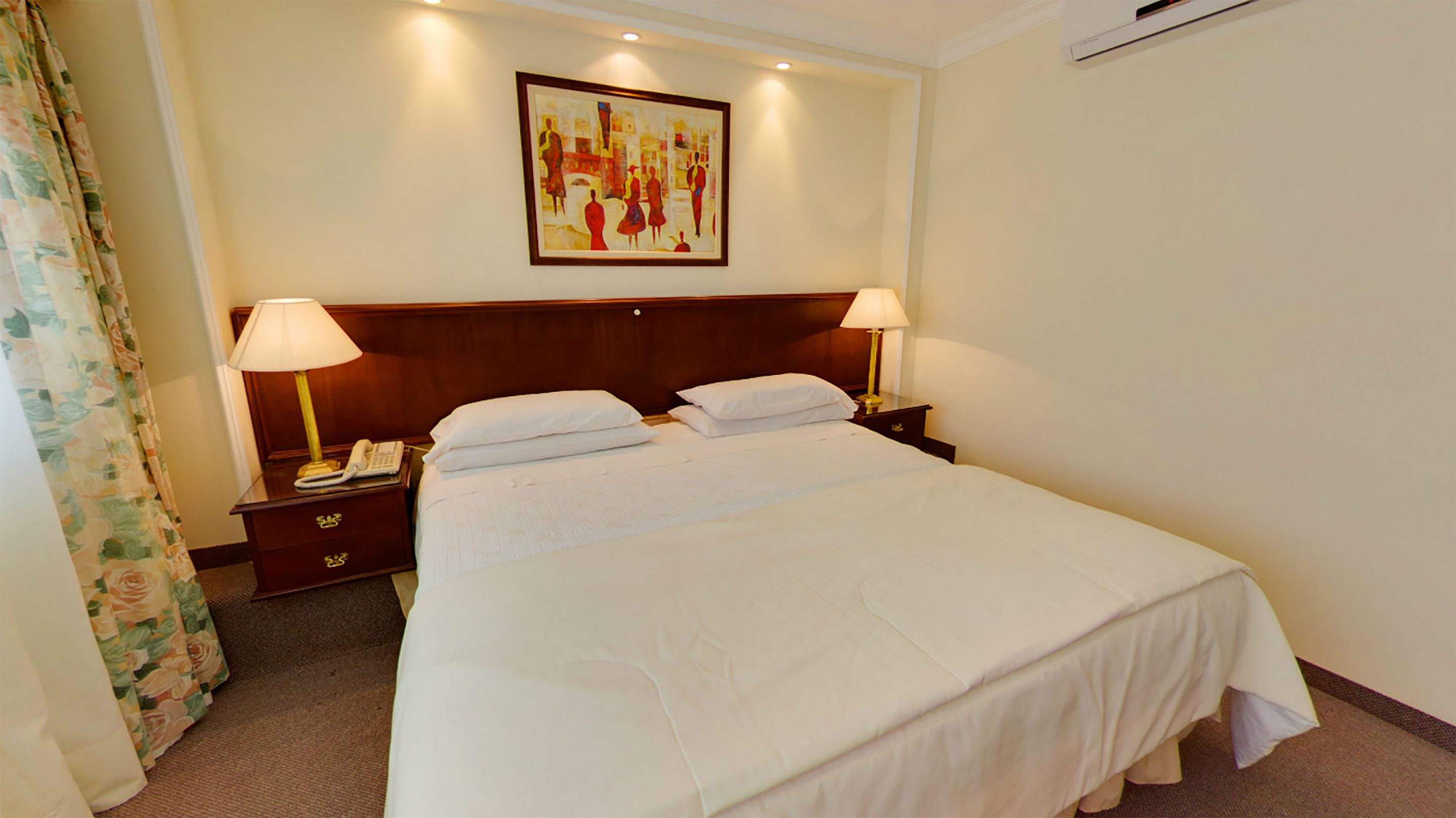 A hotel room with a large bed, two bedside lamps, a nightstand with a phone, and a painting on the wall.