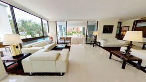 Amplia sala de estar con un ventanal, sofás blancos y una zona de comedor con sillas y una mesa.