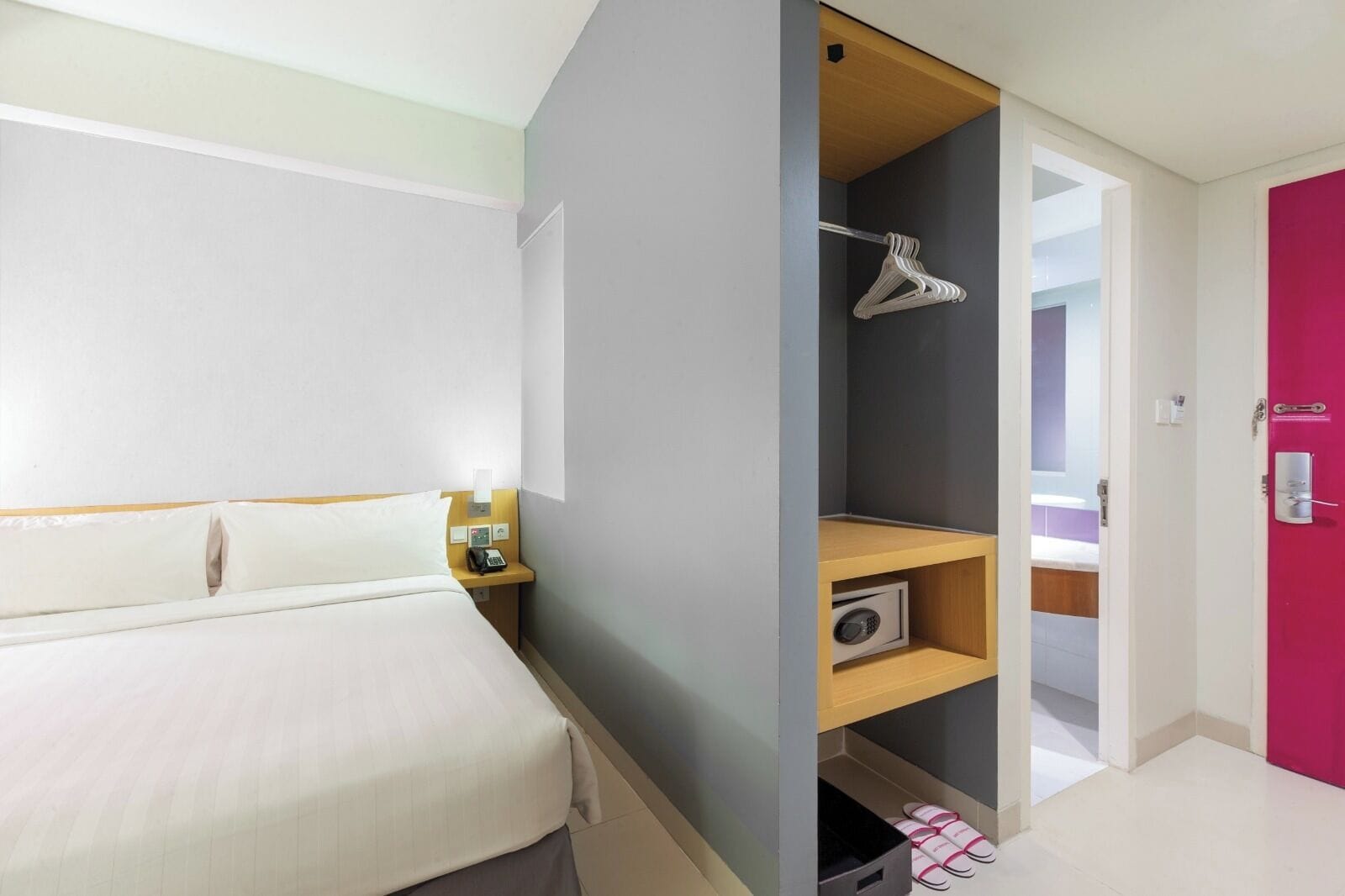 Een hotelkamer met een bed, een nachtkastje met telefoon, een plank met radio, een kledingkast en een deur.
