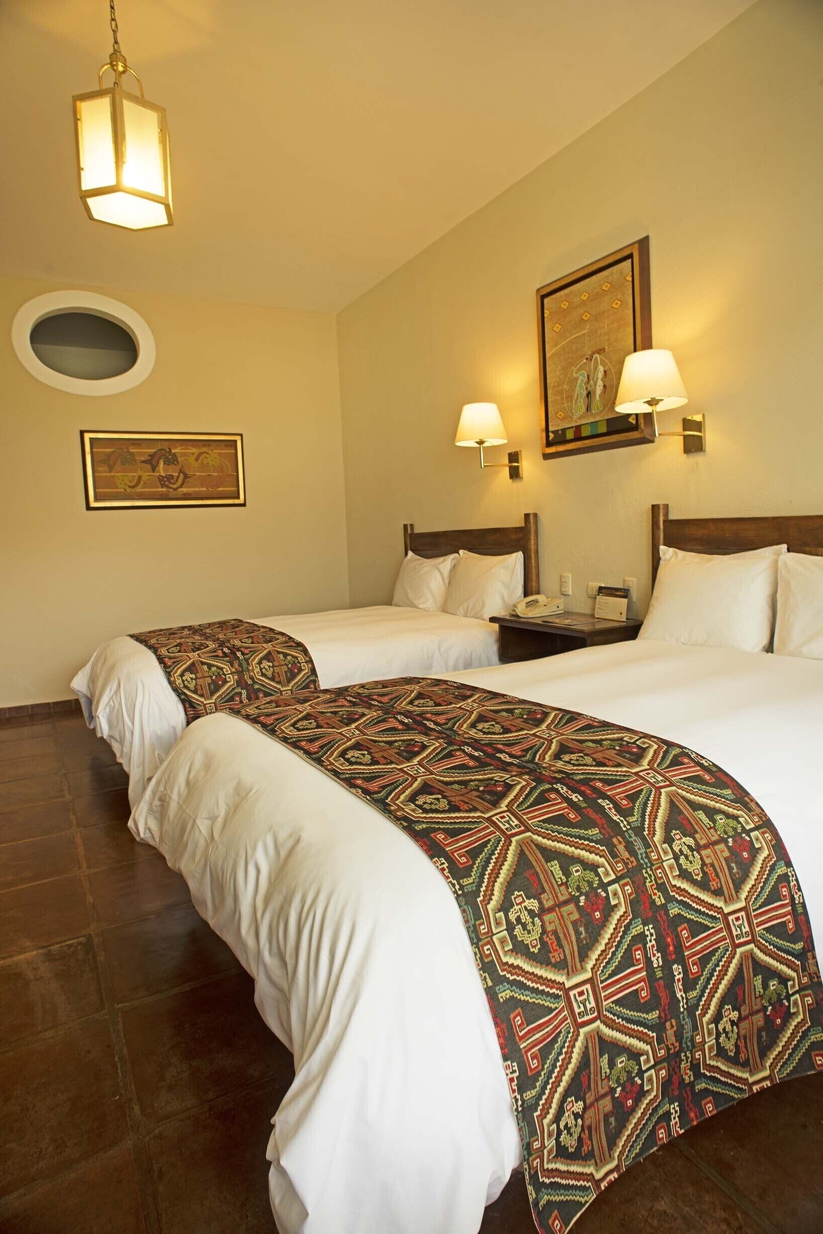 A hotel room with two beds, a nightstand, a telephone, and a wall-mounted lamp.