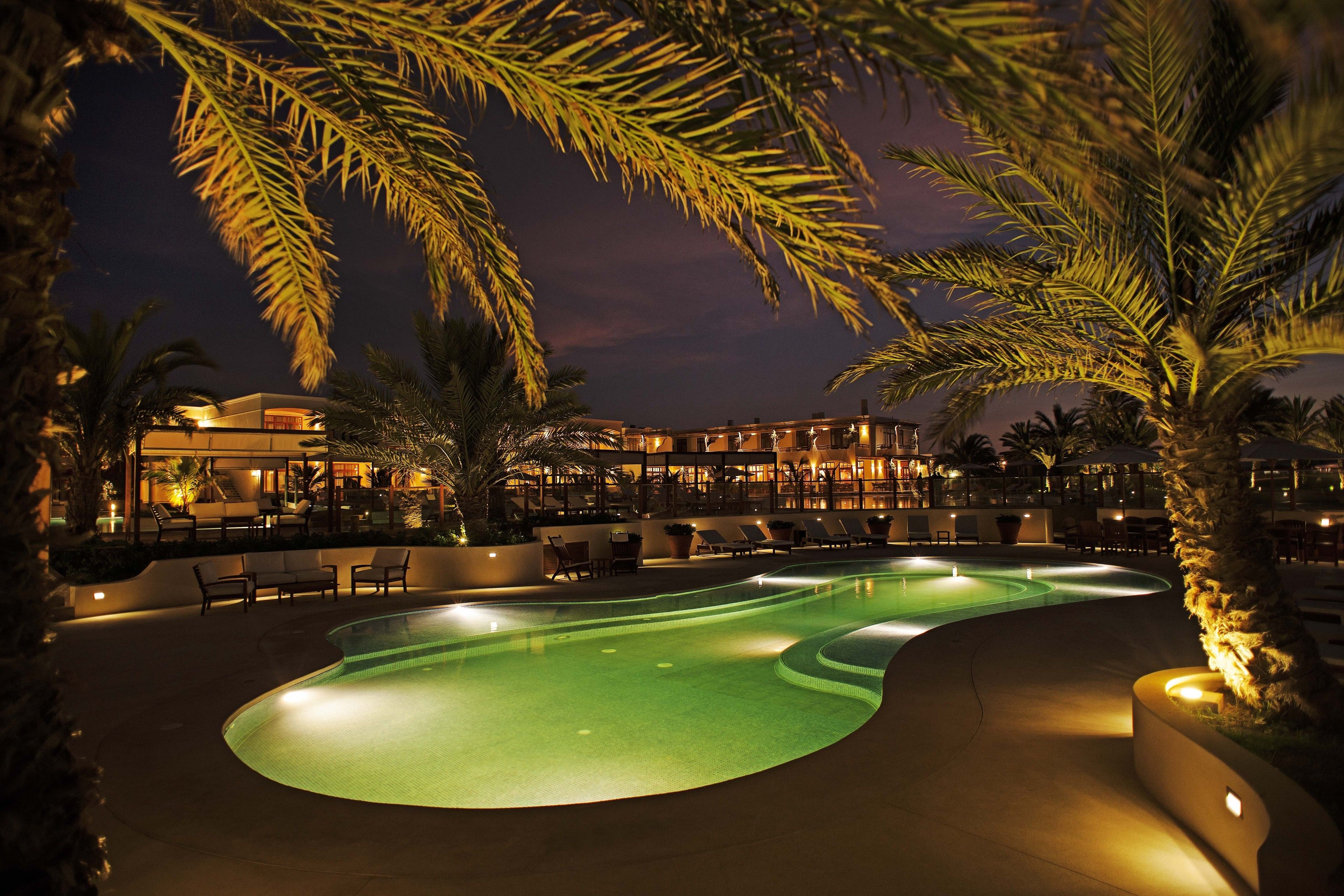 Zona de piscina nocturna amb gandules i palmeres.