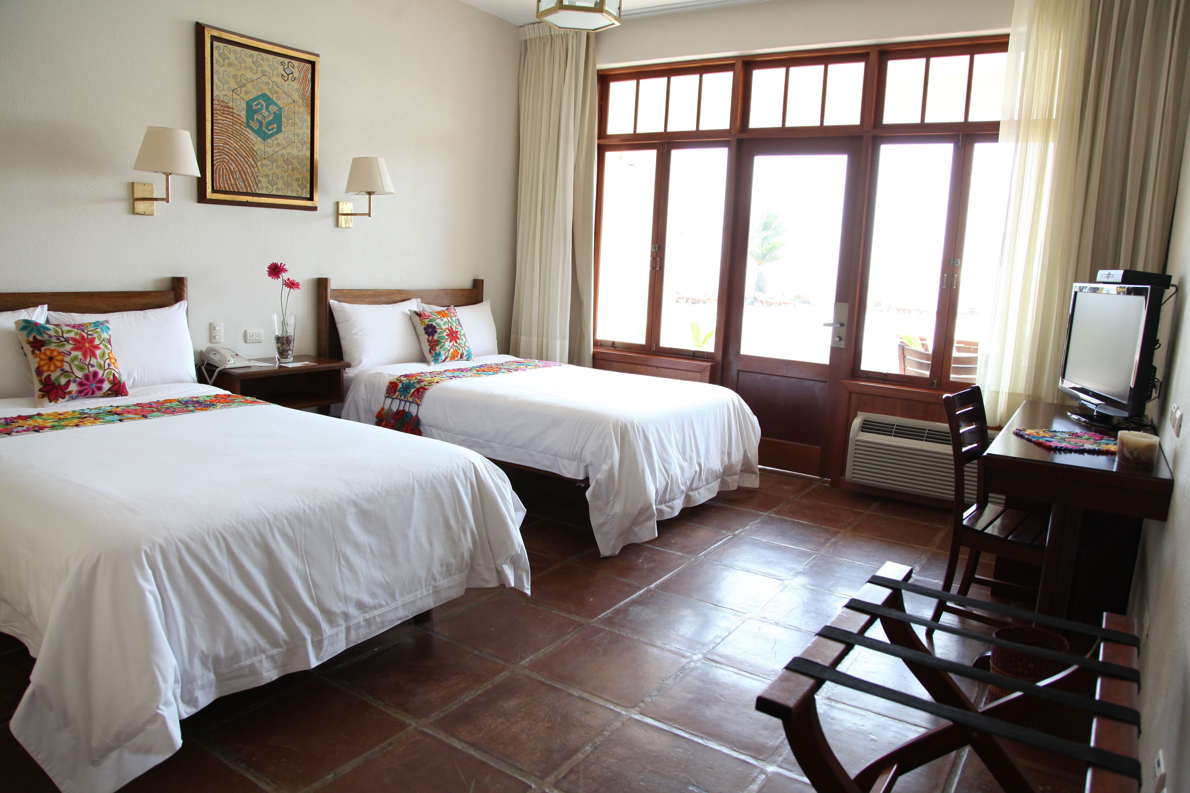 Habitación de hotel con dos camas, un escritorio con computadora y un ventanal con cortinas.