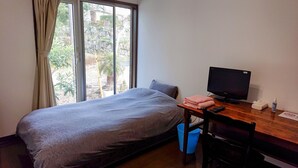 A small room with a bed, a desk with a computer, and a window with curtains. - Lilac Hotels and Resort (Kanoya)