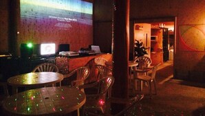 An outdoor seating area with tables and chairs, a projection screen displaying text, and a brick wall. - Lilac Hotels and Resort (Kanoya)