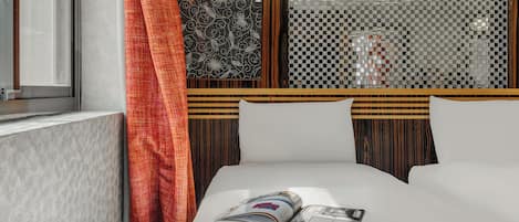 A hotel room with a bed, a window with a view, and a decorative wall panel.