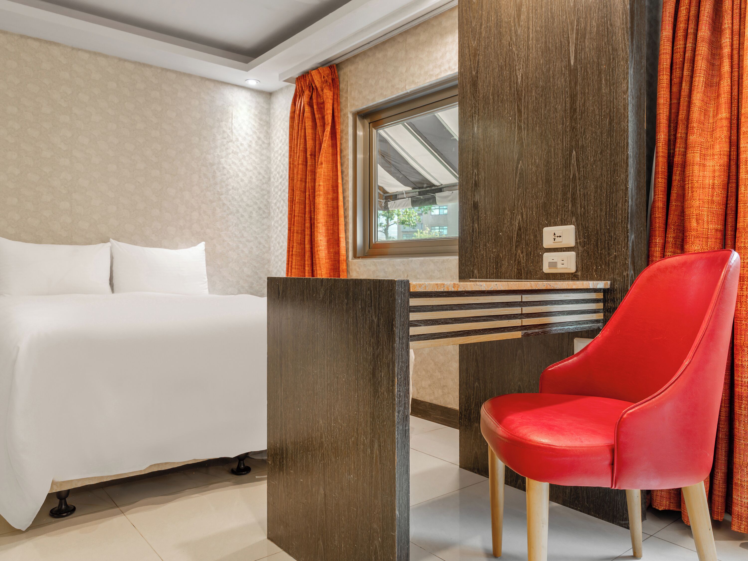 A hotel room with a bed, a desk, a chair, and a window with curtains.