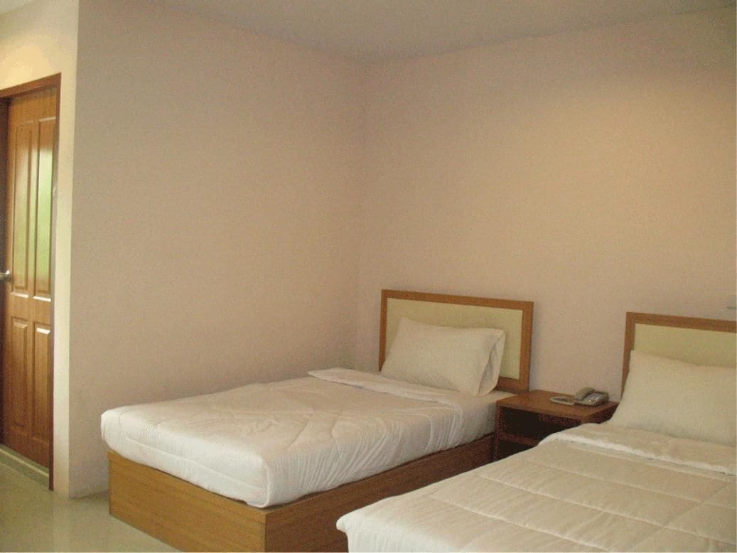 A room with two single beds, wooden headboards, a nightstand with a phone, and a wooden door.