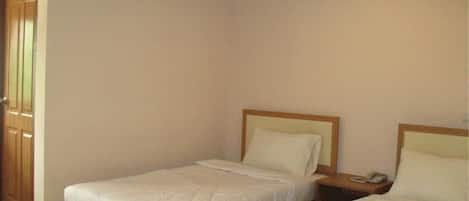 A room with two single beds, wooden headboards, a nightstand with a phone, and a wooden door.