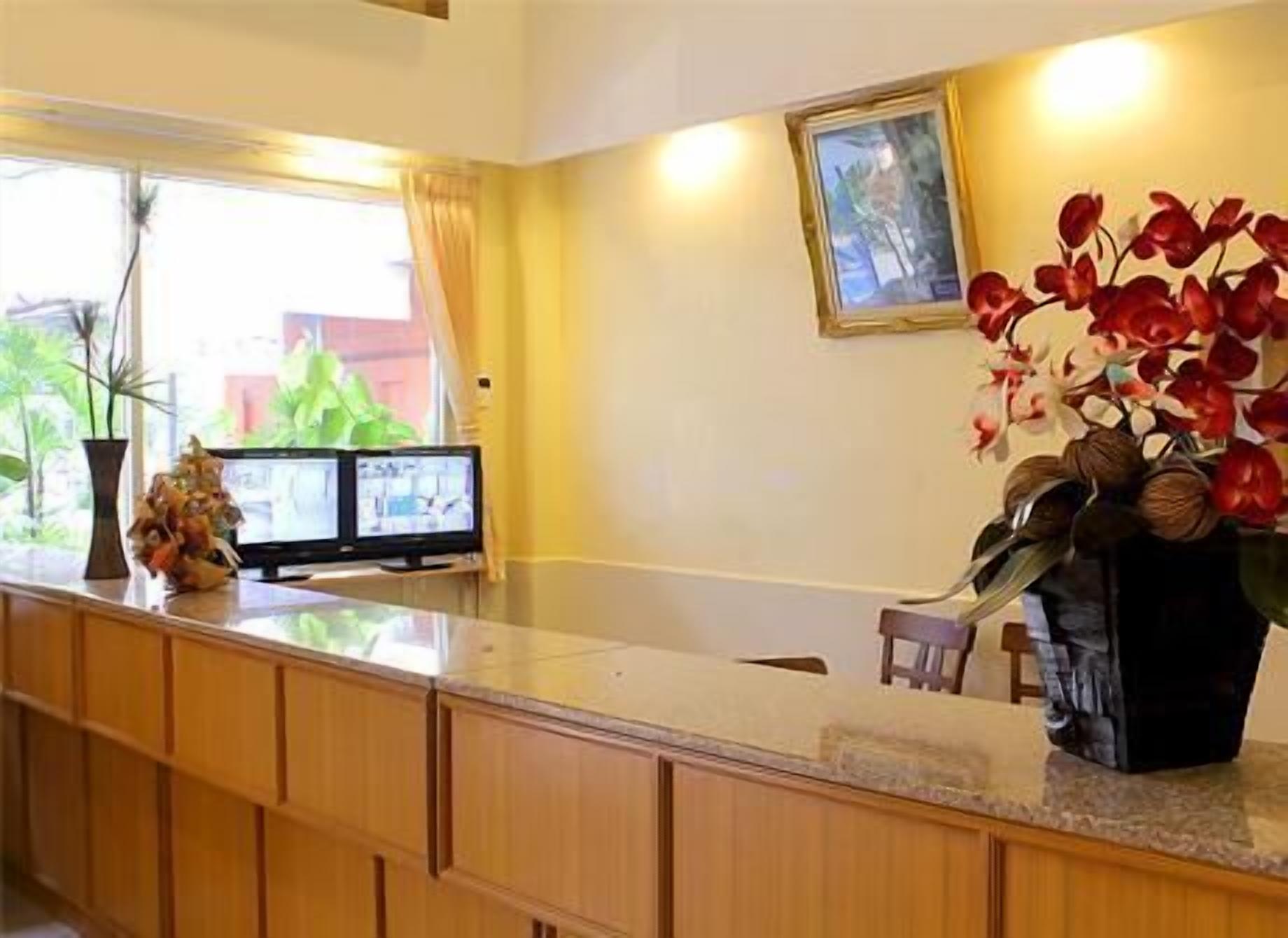 A reception area with a wooden counter, two monitors, a vase with red flowers, and a framed picture on the wall.