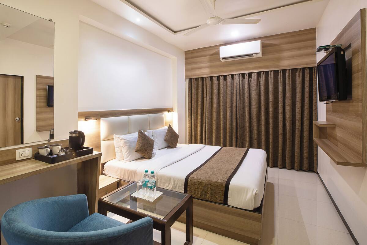 A hotel room with a bed, bedside table, chair, and a TV mounted on the wall.