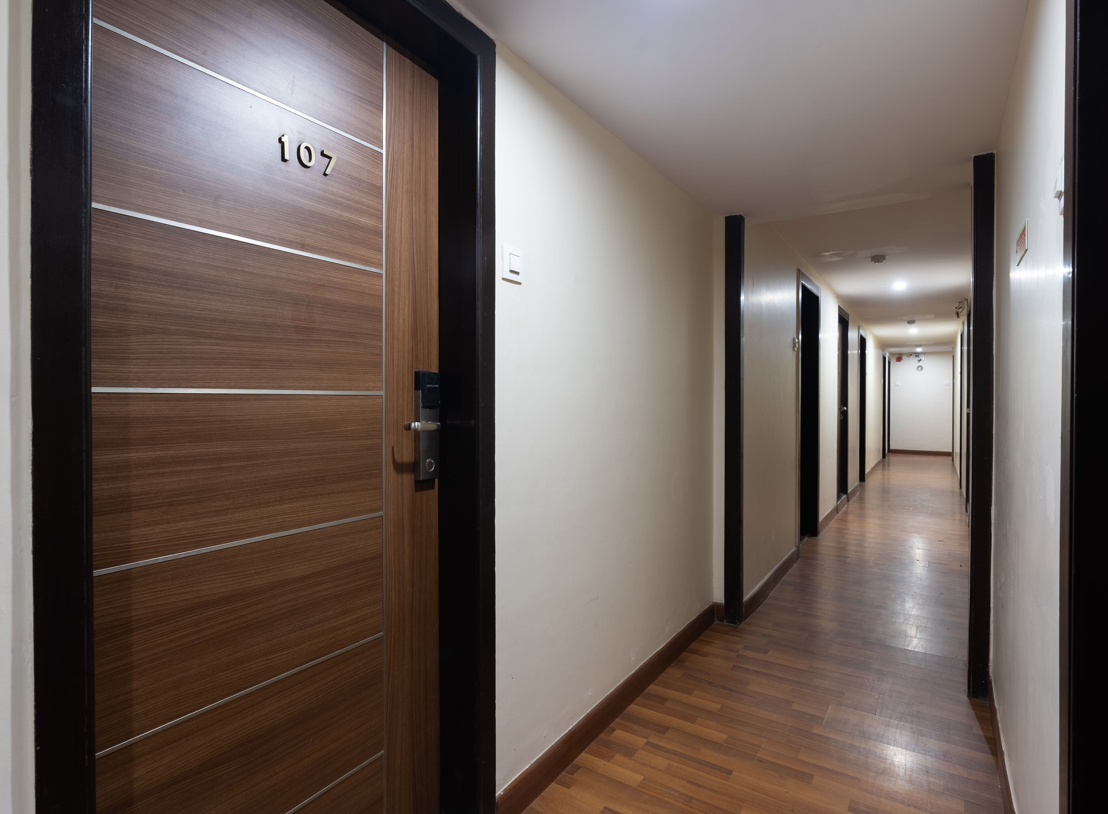 A long, narrow hallway with wooden flooring and a door labeled "107".