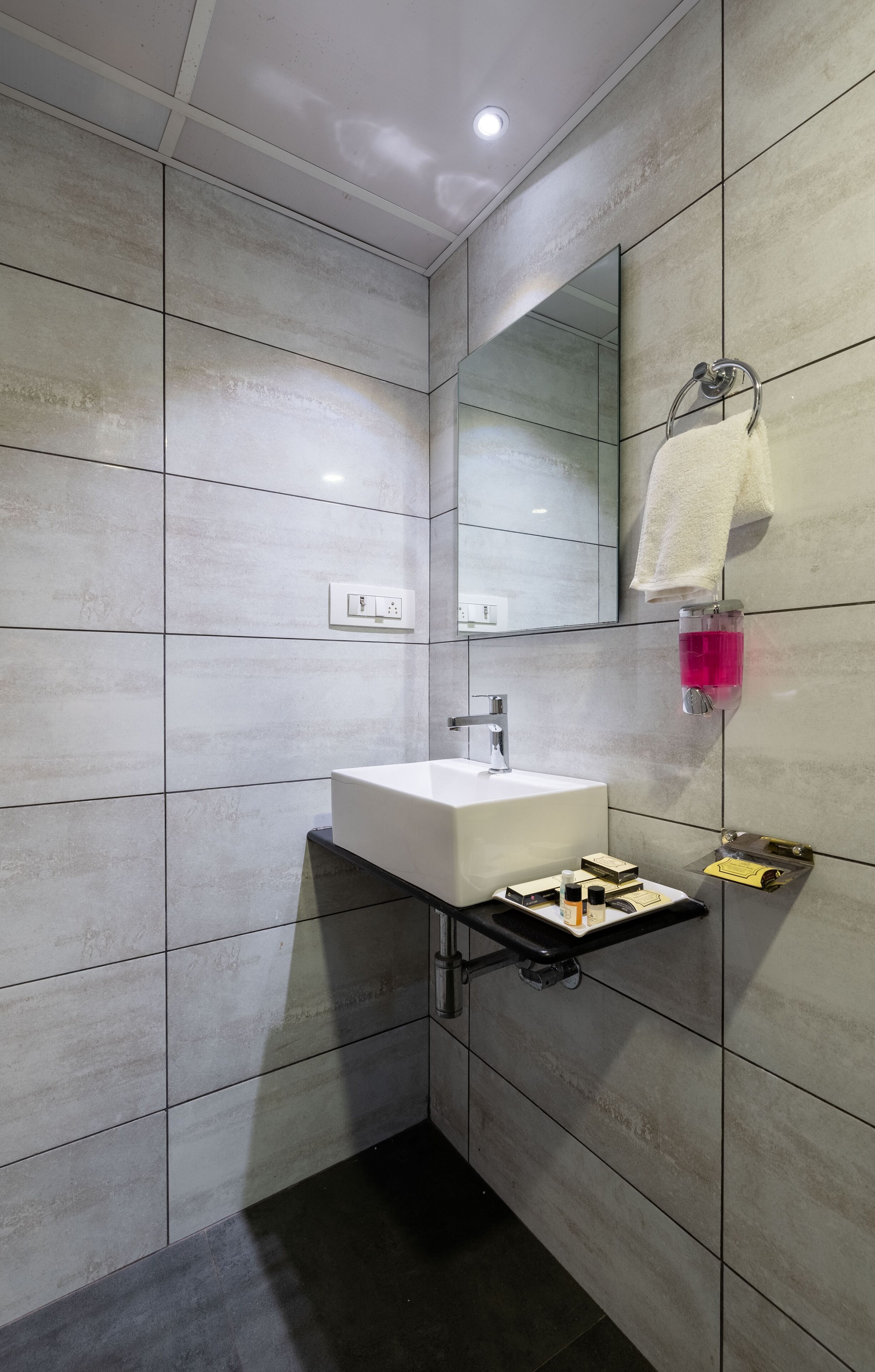 A modern bathroom with a white sink, a mirror, a towel rack, and a soap dispenser.