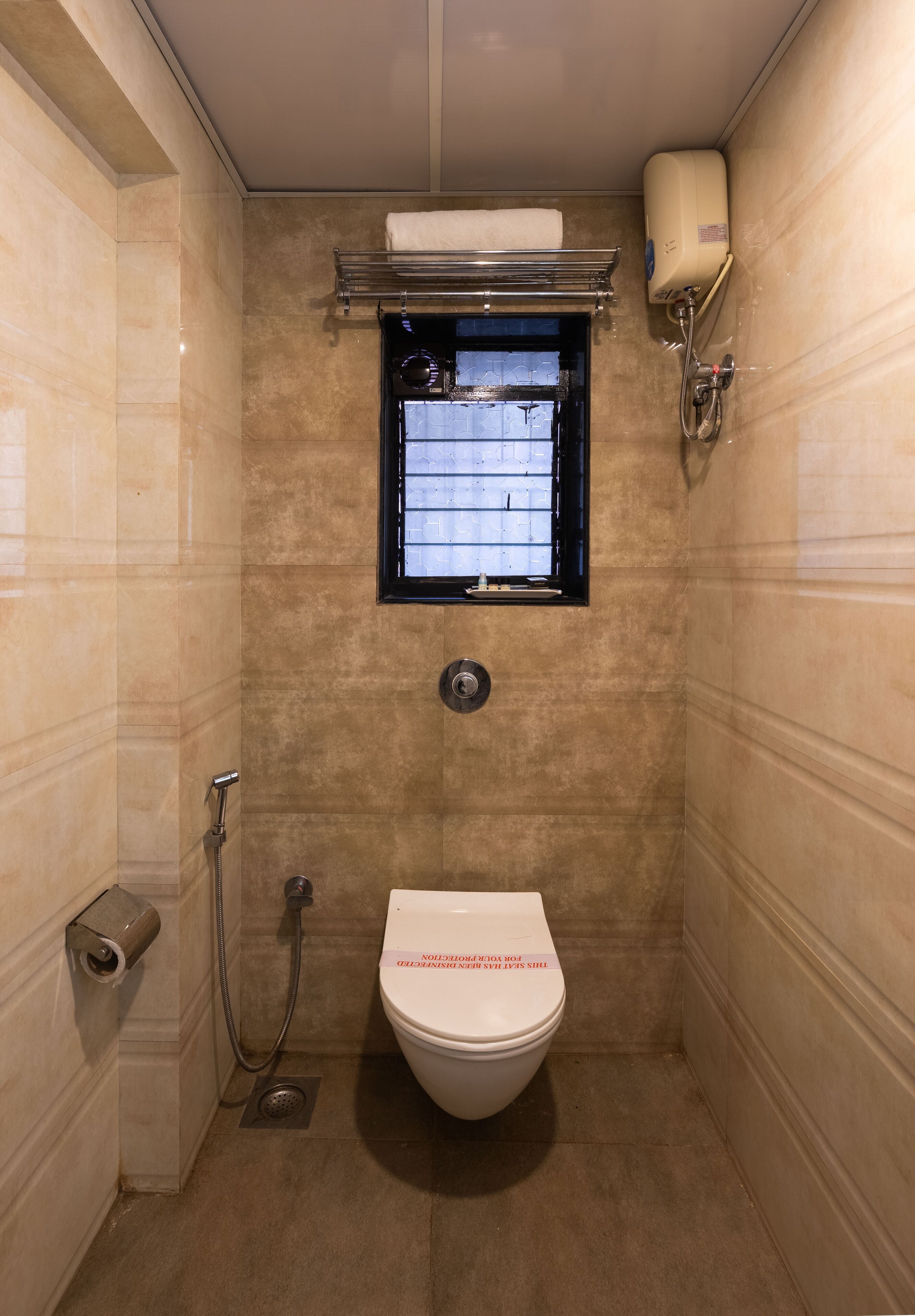 A small, tiled bathroom with a toilet, a window, and a towel rack.
