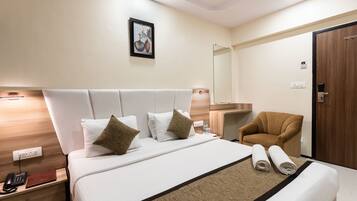 A hotel room with a large bed, a bedside table with a phone and a book, a chair, a mirror, and a wooden door.