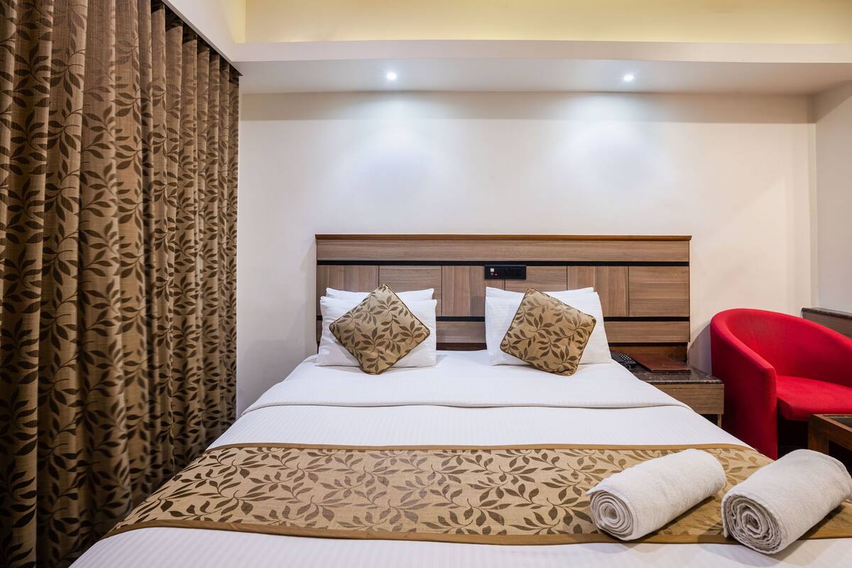 A hotel room with a large bed, two pillows, a red chair, and a wooden headboard.