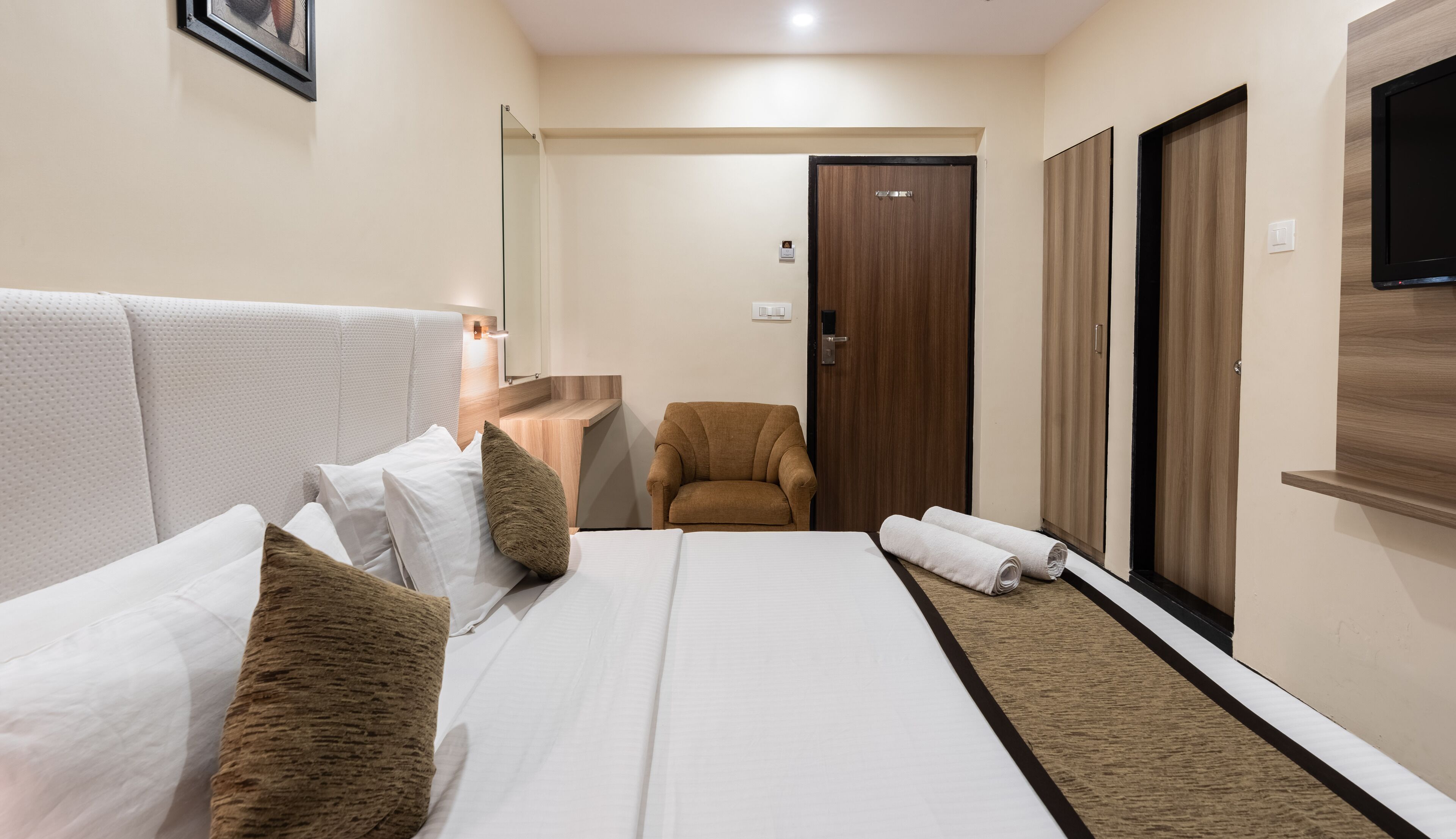 Habitación de hotel con una cama grande, una silla, un armario de madera y un televisor.