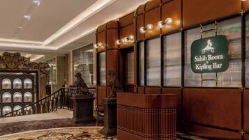 A lobby with a mahogany reception desk, a sign for the Sahib Room & Kipling Bar, and a decorative staircase.