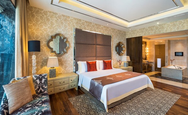 A spacious bedroom with a large bed, bedside tables, a nightstand, a mirror, and a bathroom visible through an open door.