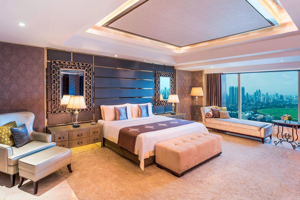 A modern hotel room with a large bed, a sofa, a desk, and a view of the cityscape.