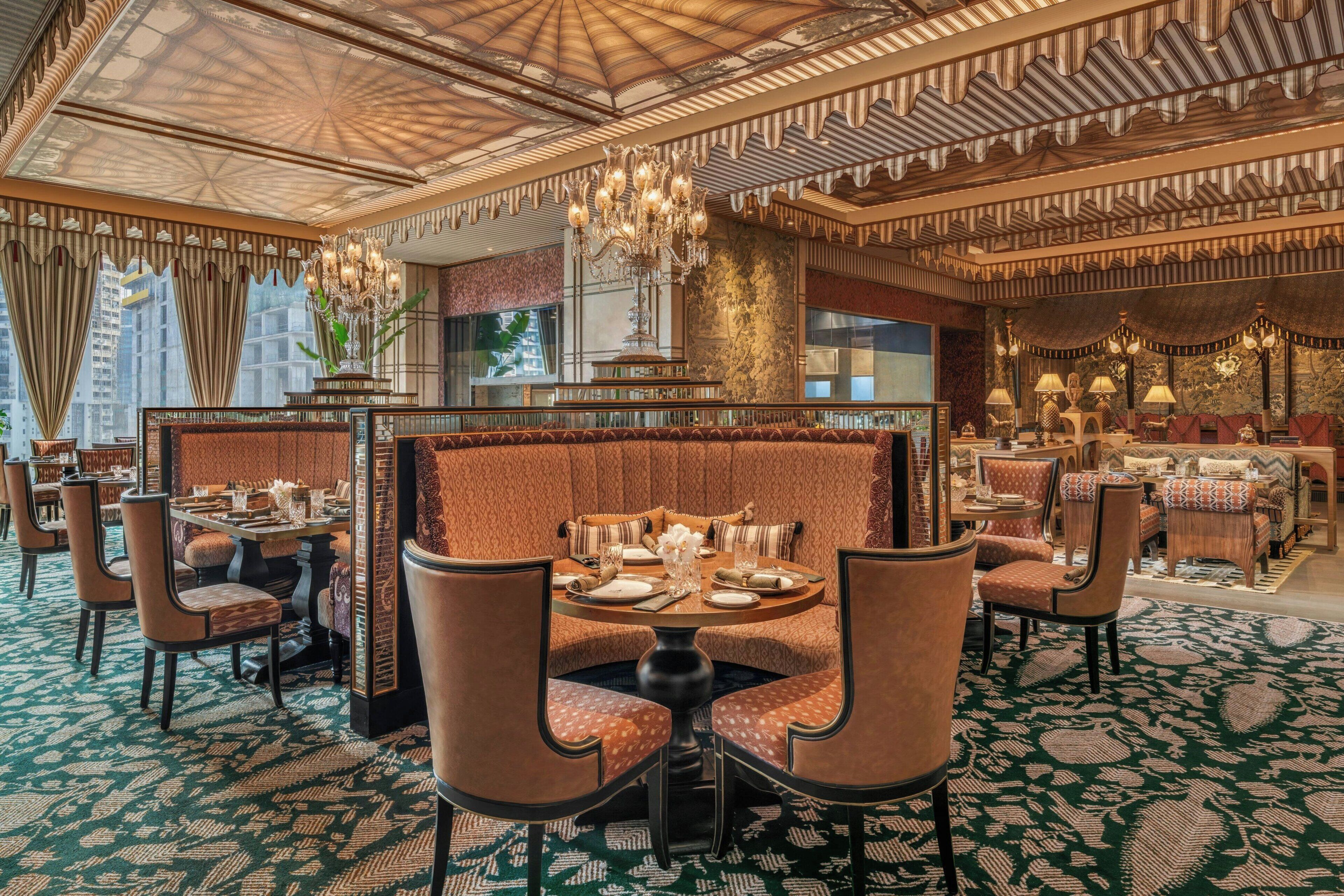 Um espaço de refeições luxuoso em hotel, com lustres ornamentados, estofados estampados e vista para a paisagem urbana.