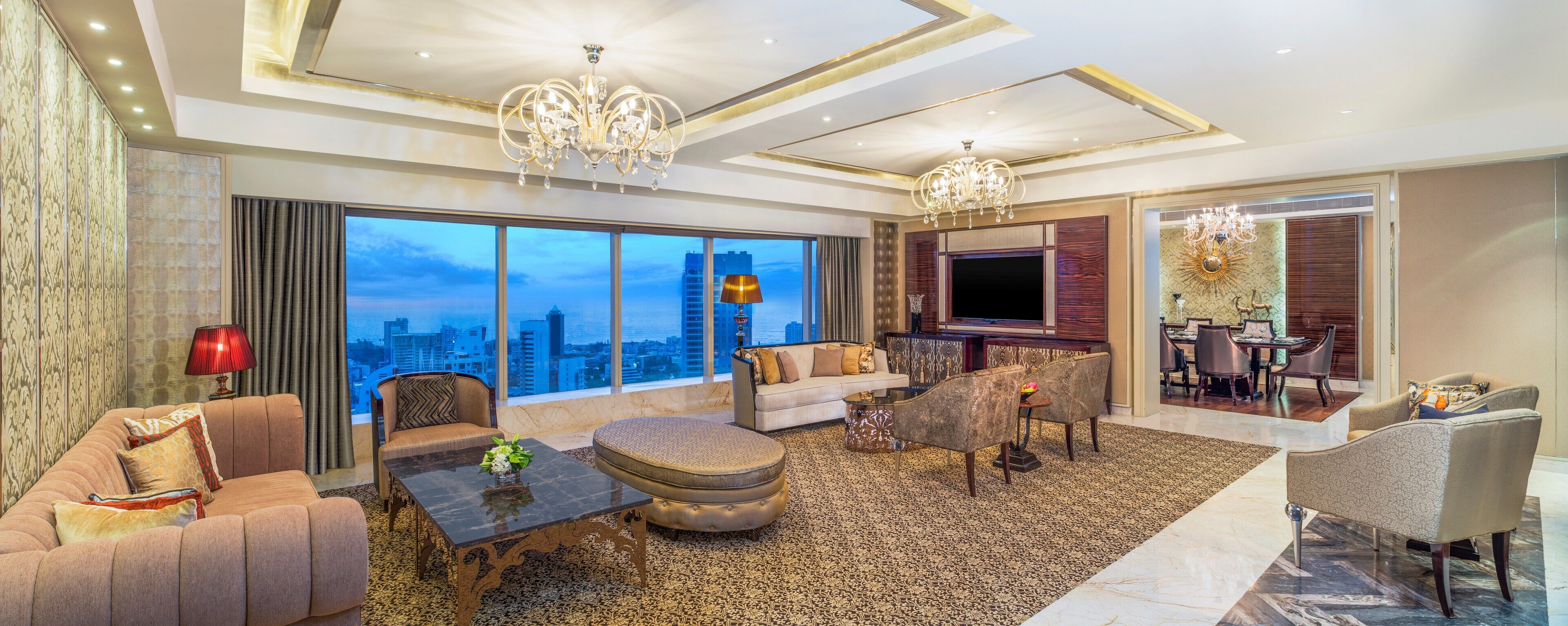 A spacious living room with a large TV, comfortable seating, a coffee table, and a view of the cityscape.