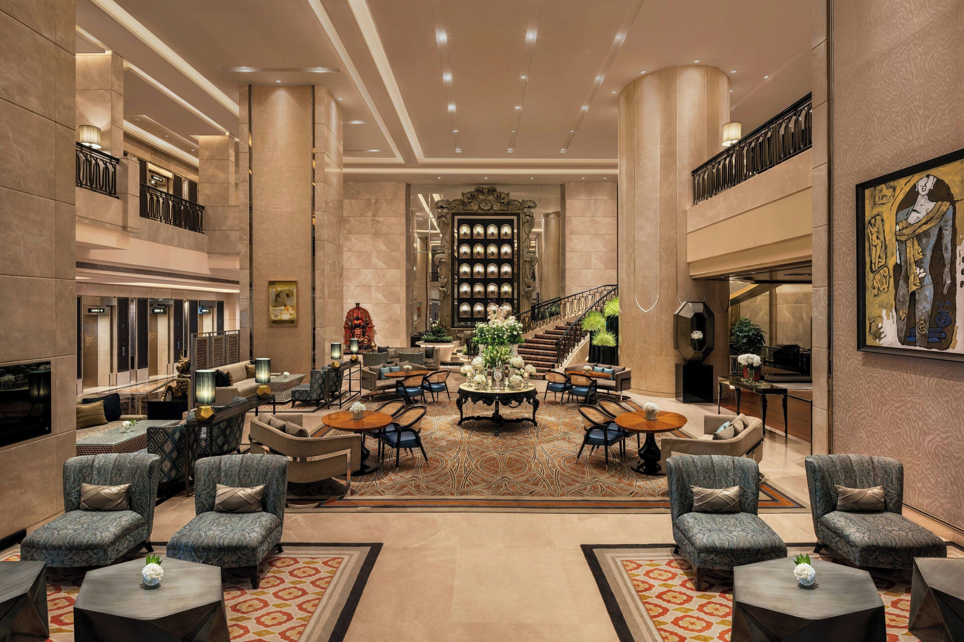 A spacious lobby with a central seating area, a staircase, and a large painting on the wall.