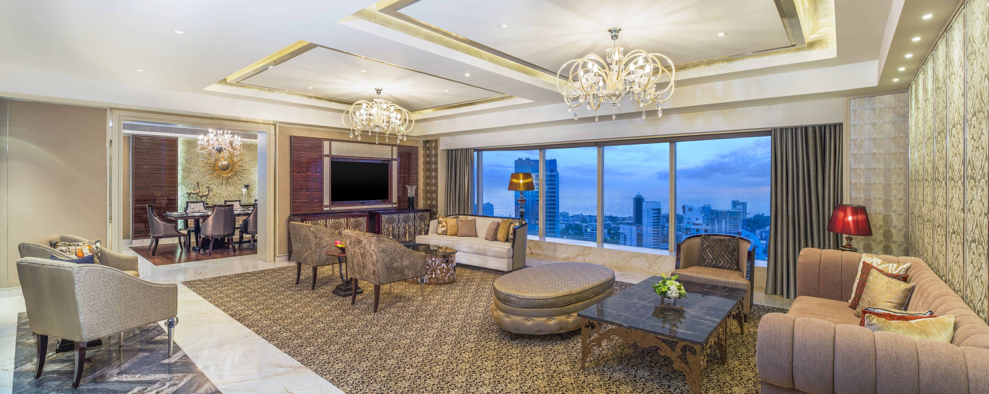 A spacious living room with a large window, a chandelier, and a television.