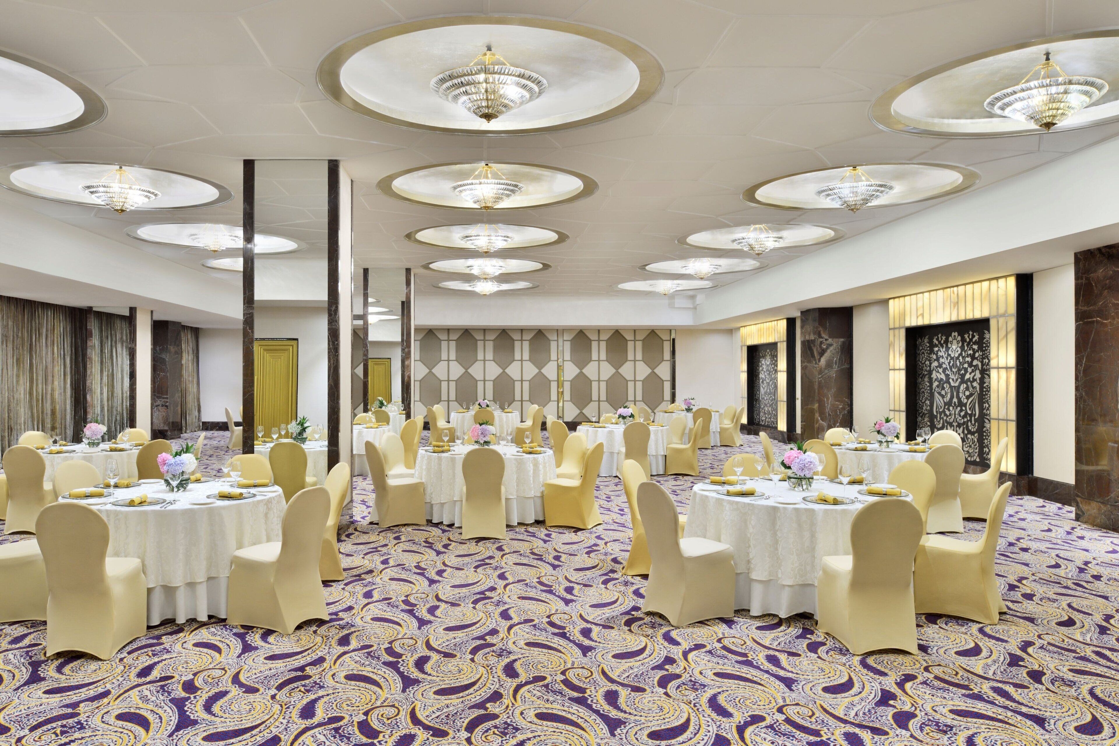 A banquet hall with round tables, chairs, and chandeliers.